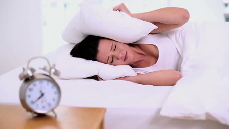Exhausted-woman-lying-on-her-bed-covering-her-ears-