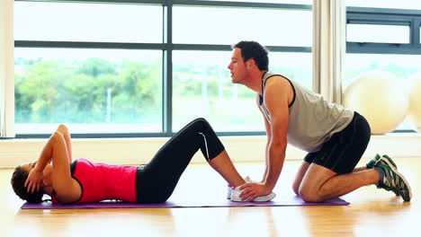 Handsome-coach-supporting-young-woman-doing-situps