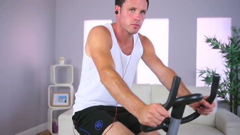 Handsome-sporty-man-training-on-exercise-bike-and-listening-to-music