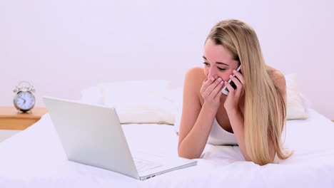 Glücklich-Wunderschöne-Blondine-Liegt-Auf-Dem-Bett-Telefonierend-Und-Mit-Laptop