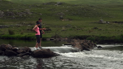 Pareja-Parada-Sobre-Rocas-En-Medio-De-Un-Río