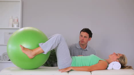 Physiotherapist-watching-his-patient-move-an-exercise-ball-in-between-her-knees