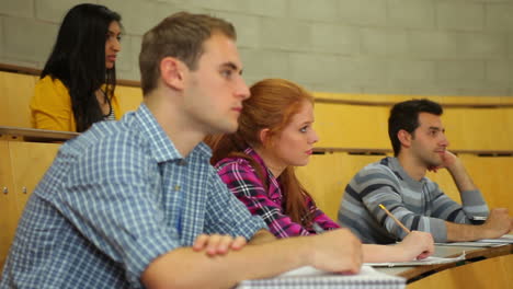 Estudiantes-Enfocados-Escuchando-En-La-Sala-De-Conferencias-Y-Tomando-Notas