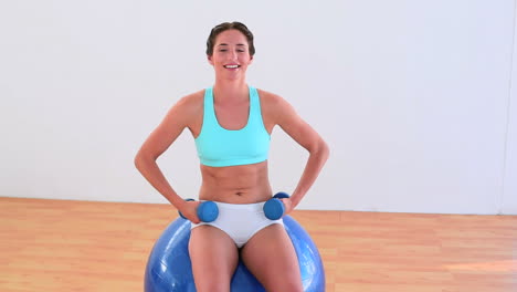 Fit-brunette-sitting-on-an-exercise-ball-and-lifting-weights