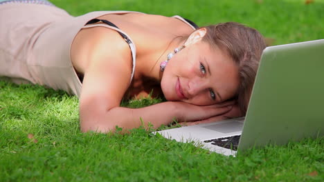 Happy-student-lying-on-grass-looking-at-laptop