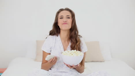 Young-woman-eating-bowl-of-popcorn-on-bed-and-watching-tv