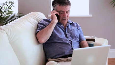 Annoyed-man-talking-on-the-phone-on-the-sofa-with-his-laptop