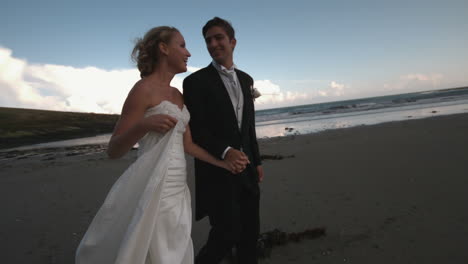 Cheerful-newlywed-couple-walking-and-kissing-on-the-beach