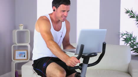 Attractive-sporty-man-exercising-on-bike-and-using-laptop