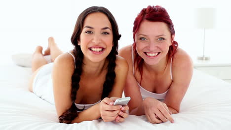 Cheerful-laughing-women-holding-a-smartphone-lying-on-bed