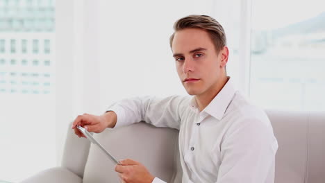 Serious-young-man-using-his-tablet-sitting-on-couch