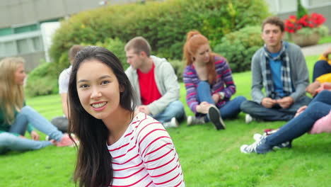 Student-smiling-at-camera-with-friends-behind-her-on-grass