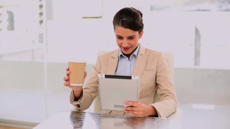 Smiling-beautiful-businesswoman-using-a-laptop-while-drinking-coffee