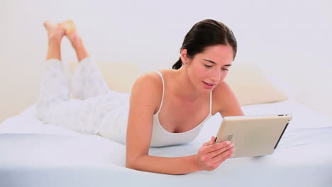 Attraktive-Brünette-Mit-Ihrem-Digitalen-Tablet-Auf-Dem-Bett-Liegend