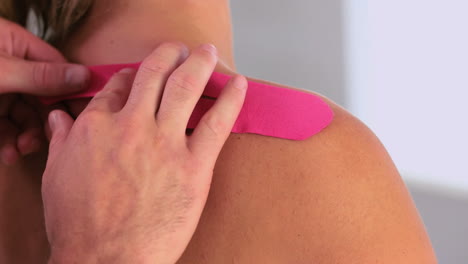 Physiotherapist-applying-pink-kinesio-tape-to-patients-back