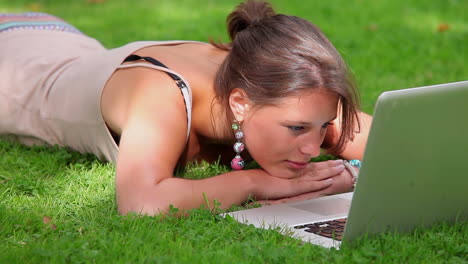 Smiling-student-lying-on-grass-looking-at-laptop