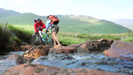 Couple-crossing-a-stream-together-with-their-bikes