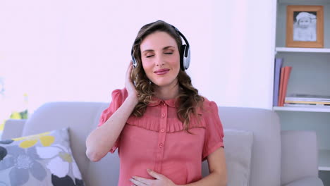 Modelo-Bastante-Embarazada-Sentada-En-Su-Sofá-Escuchando-Música