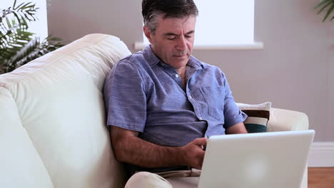 Mature-man-sitting-on-the-couch-using-laptop-and-answering-his-phone