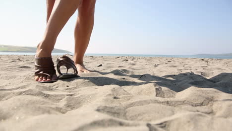Woman-putting-on-sandals-on-the-beach