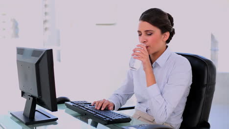 Calm-beautiful-businesswoman-drinking-water-while-using-computer