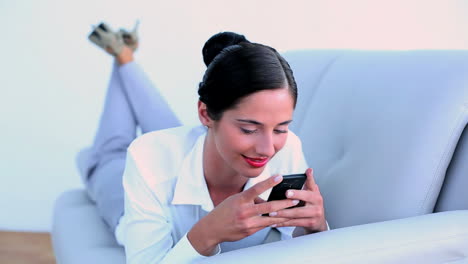 Attractive-businesswoman-lying-on-couch-and-sending-a-text-message