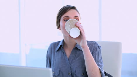 Happy-businesswoman-working-on-a-laptop-having-a-coffee