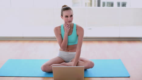 Fit-model-sitting-on-exercise-mat-using-her-laptop