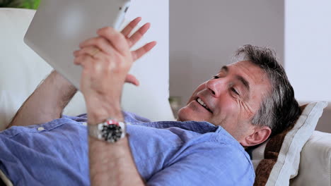 Mature-man-lying-on-the-sofa-using-his-digital-tablet