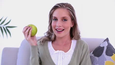 Cheerful-lovely-woman-showing-a-green-apple