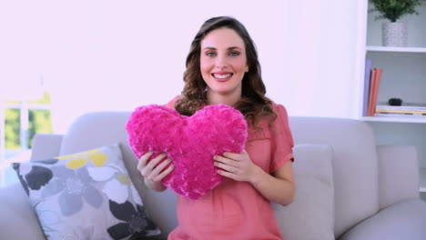 Pretty-pregnant-model-sitting-on-her-couch-hugging-a-heart-pillow
