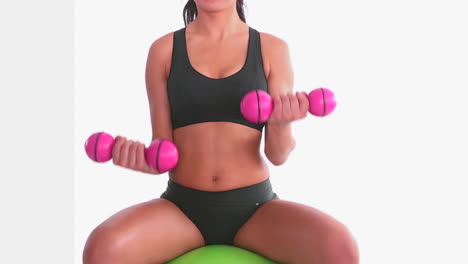Toned-woman-sitting-on-exercise-ball-training-with-dumbbells