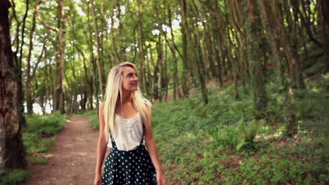 Attractive-happy-blonde-walking-on-pathway-through-forest