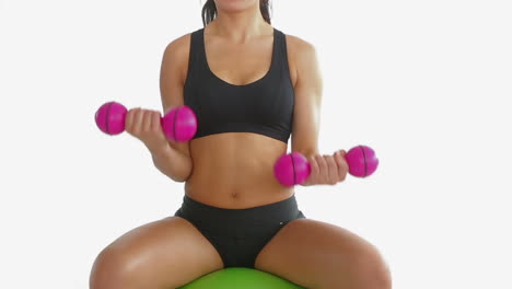 Toned-brunette-sitting-on-exercise-ball-training-with-dumbbells