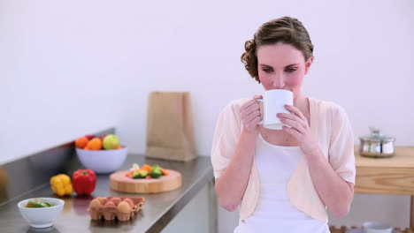 Pretty-model-standing-in-kitchen-drinking-mug-of-coffee