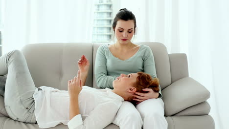 Young-calm-woman-lying-on-couch-with-her-head-on-the-lap-of-her-friend