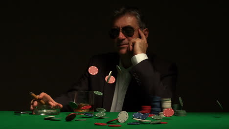 Smiling-gambler-sitting-at-table-with-chips-falling