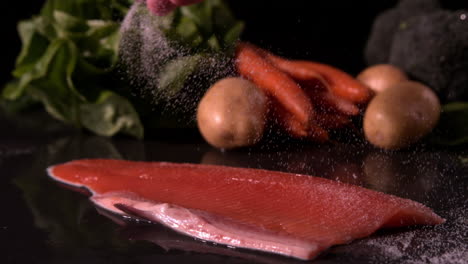 Hand-seasoning-trout-fillet-in-front-of-vegetable-selection