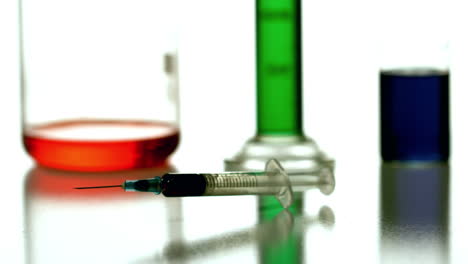 Syringe-falling-with-chemicals-in-background