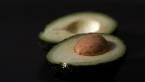 Water-dropping-on-avocado-half-against-black-background