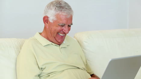 Senior-man-sitting-on-sofa-using-laptop