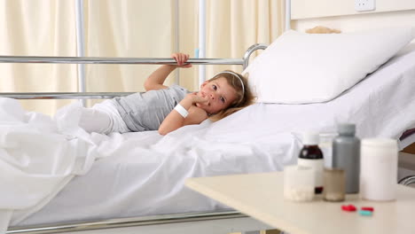 Little-girl-lying-in-hospital-bed-looking-at-medicine