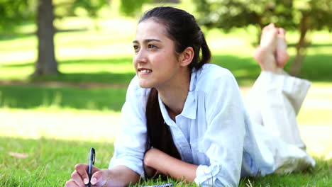 Pretty-girl-lying-on-the-grass-writing-on-notepad