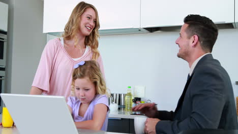 Mother-and-father-laughing-together-while-daughter-uses-laptop
