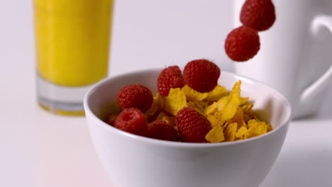 Raspberries-pouring-into-cereal-bowl-at-breakfast-table