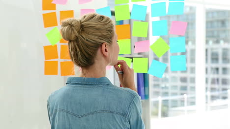 Blonde-designer-looking-at-post-its-on-window