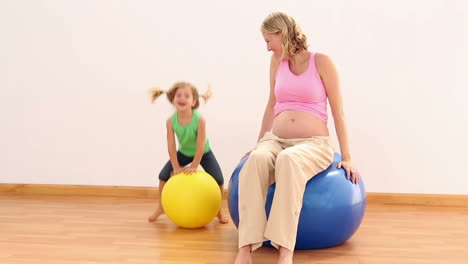 Blonde-pregnant-woman-sitting-on-exercise-ball-with-her-little-girl