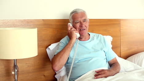 Älterer-Mann-Sitzt-Im-Bett-Und-Beantwortet-Das-Telefon