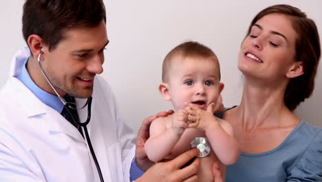 Pretty-mother-holding-baby-boy-while-pediatrician-listens-to-his-chest
