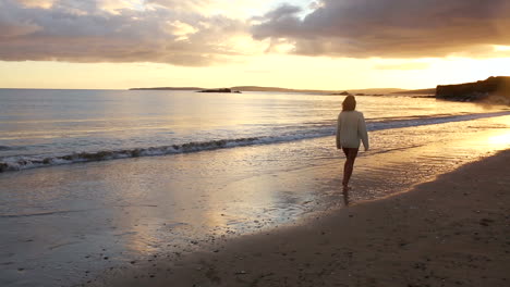 Woman-strolling-along-the-water-at-sunset